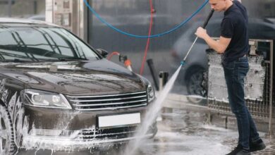 a man in dark blue shirt and jeans pant using cordless pressure to clean black car.