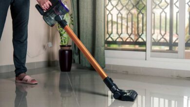 a man in balck pant and gry sanddle using cordless stick vacuum on a white floor.