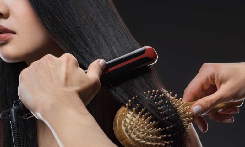 a person brushing girl black hair with hair straightener and brush