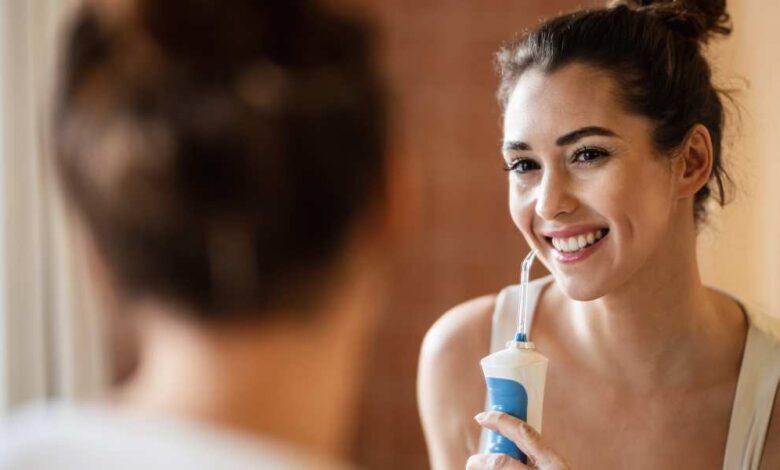 a girl using waterpik water flosser standing in front of mirror.