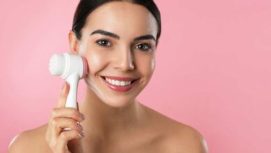 A girl using facial cleansing brushes, smiling at camera.